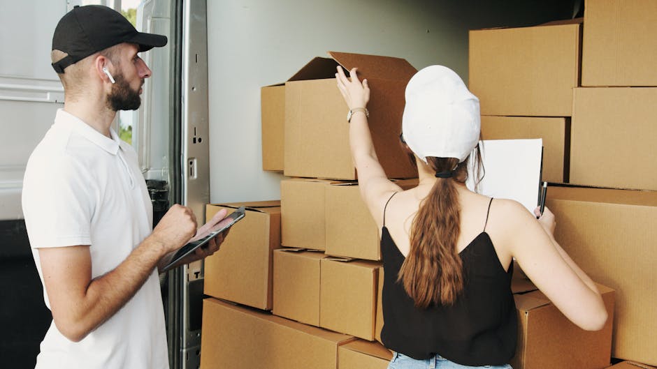 A woman with long dark hair looking inside an open cardboard box held by a man during a home relocation process. The cardboard box appears to contain packing materials or items for moving. They are in
